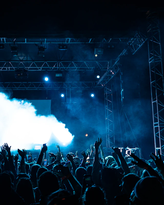 A packed crowd facing a stage under blue lights and spotlights