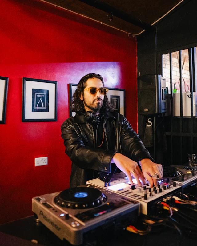 A DJ in sunglasses mixing in front of a red wall